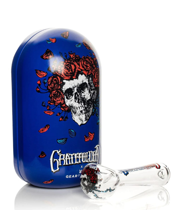 Blue Grateful Dead Bertha collectible tin with skull and roses design next to glass spoon pipe