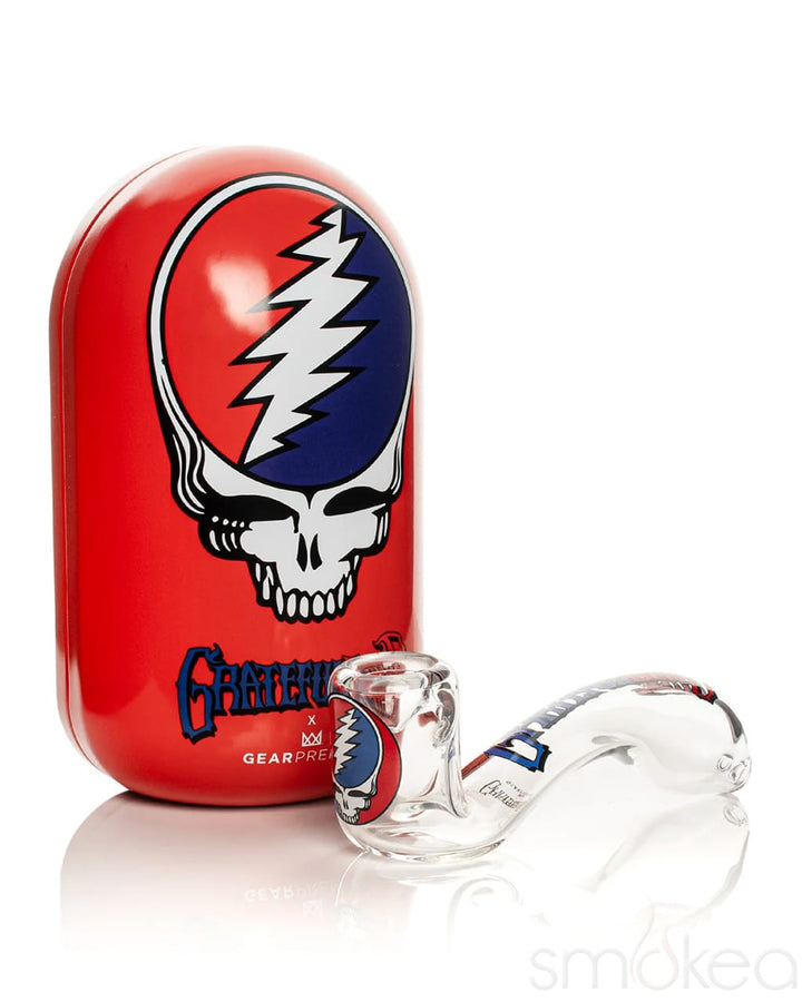 A clear glass water pipe with a red, white, and blue Grateful Dead skull design, shown next to its red oval carrying case featuring the Grateful Dead logo.